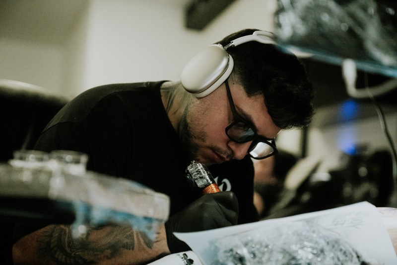 Sadone concentrating while working with a tattoo machine, surrounded by his working materials.