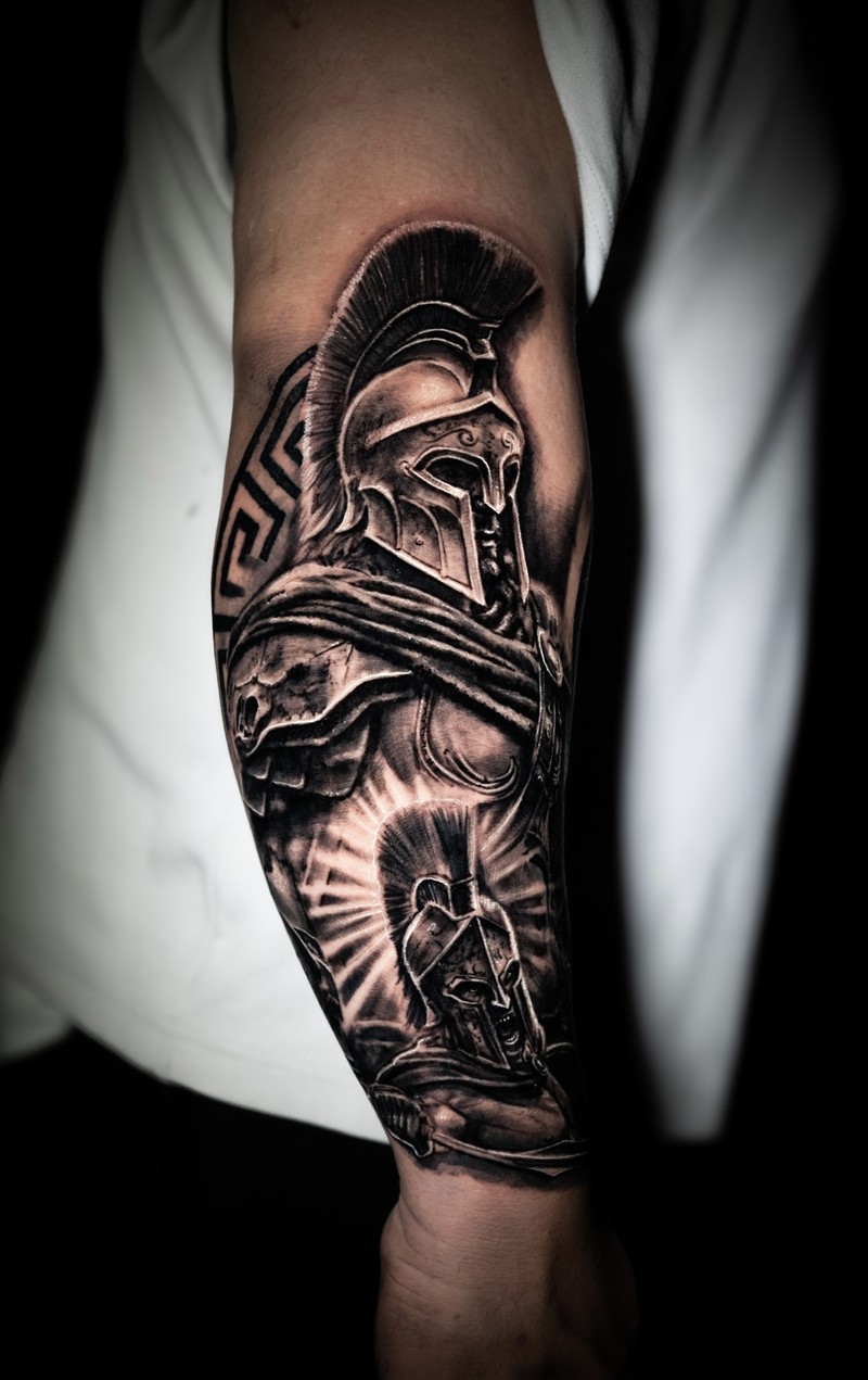 Black and grey forearm tattoo with two armored warriors, detailed helmets and draped fabric.